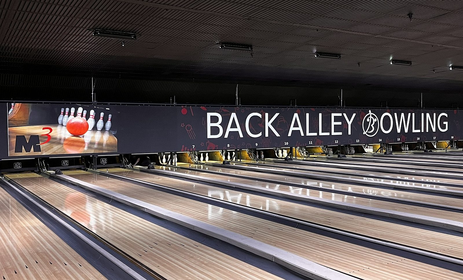 Bowling lanes with an M3 Office sign featuring a bowling ball hitting pins.